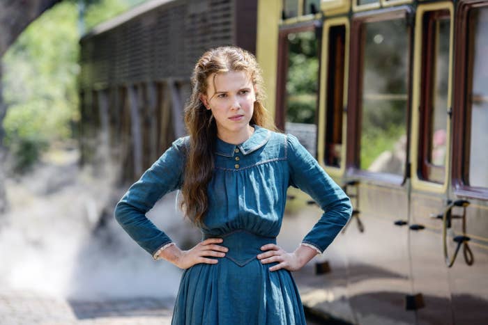 Millie acting in a scene with a train wearing a long denim dress