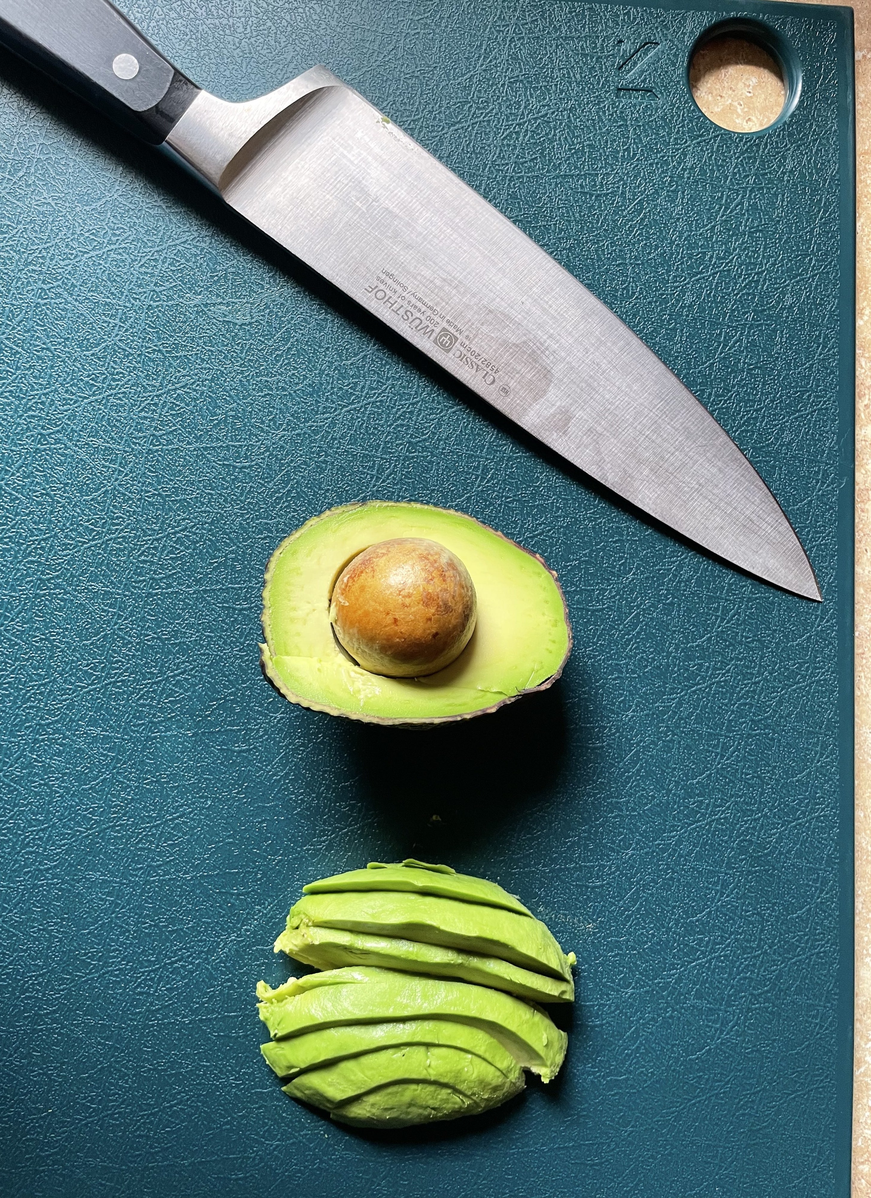 turquoise cutting board with sliced avocado and knife