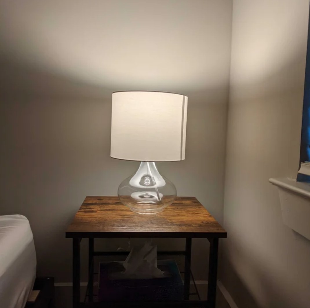 Clear glass base lamp with beige shade on wooden table