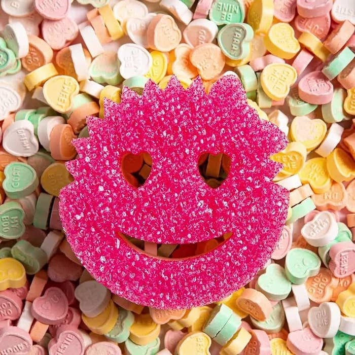 a smiley face shaped cleaning sponge on a bed of heart candies