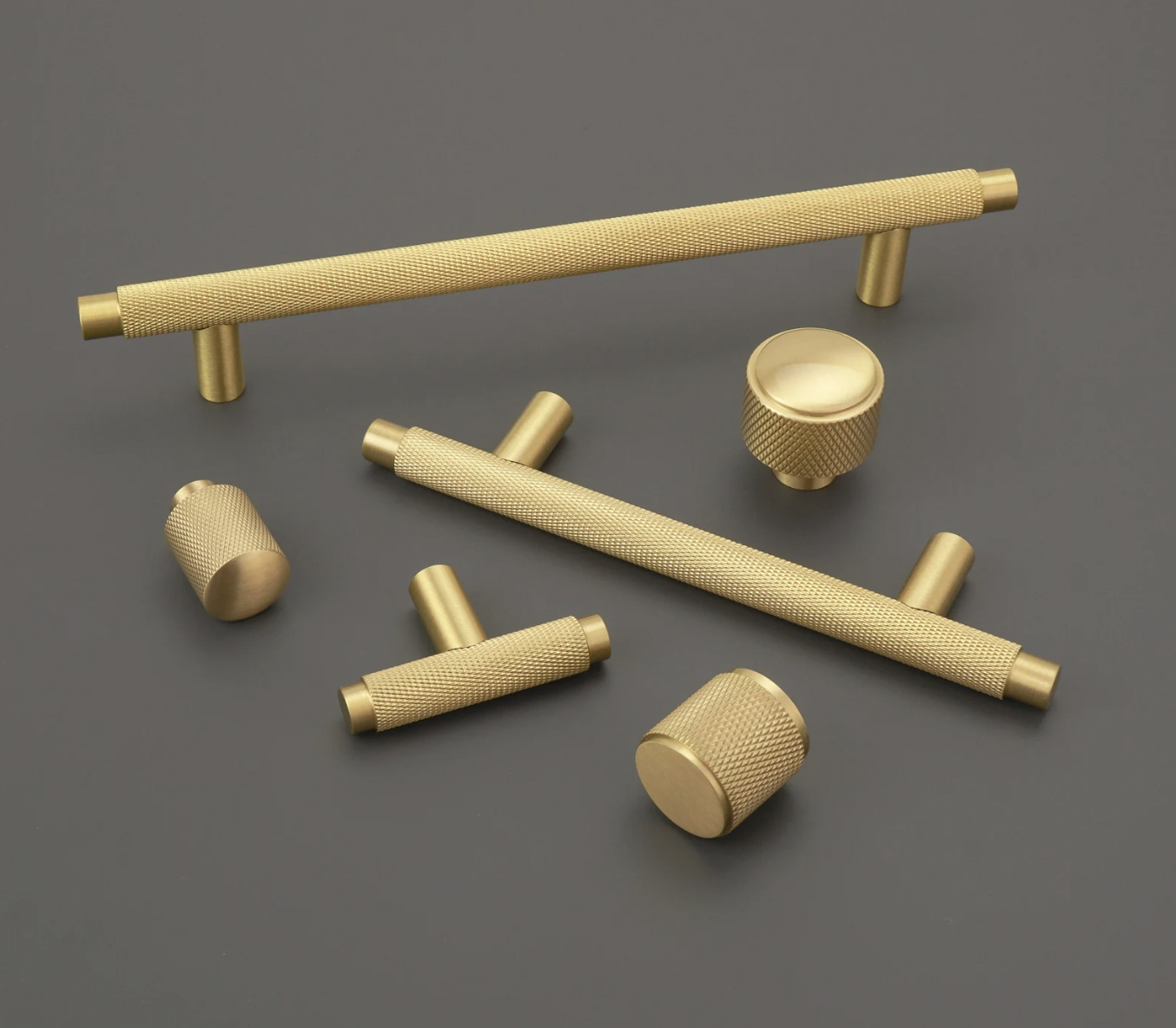 two knurled solid brass pulls and three knurled solid brass knobs on a gray surface
