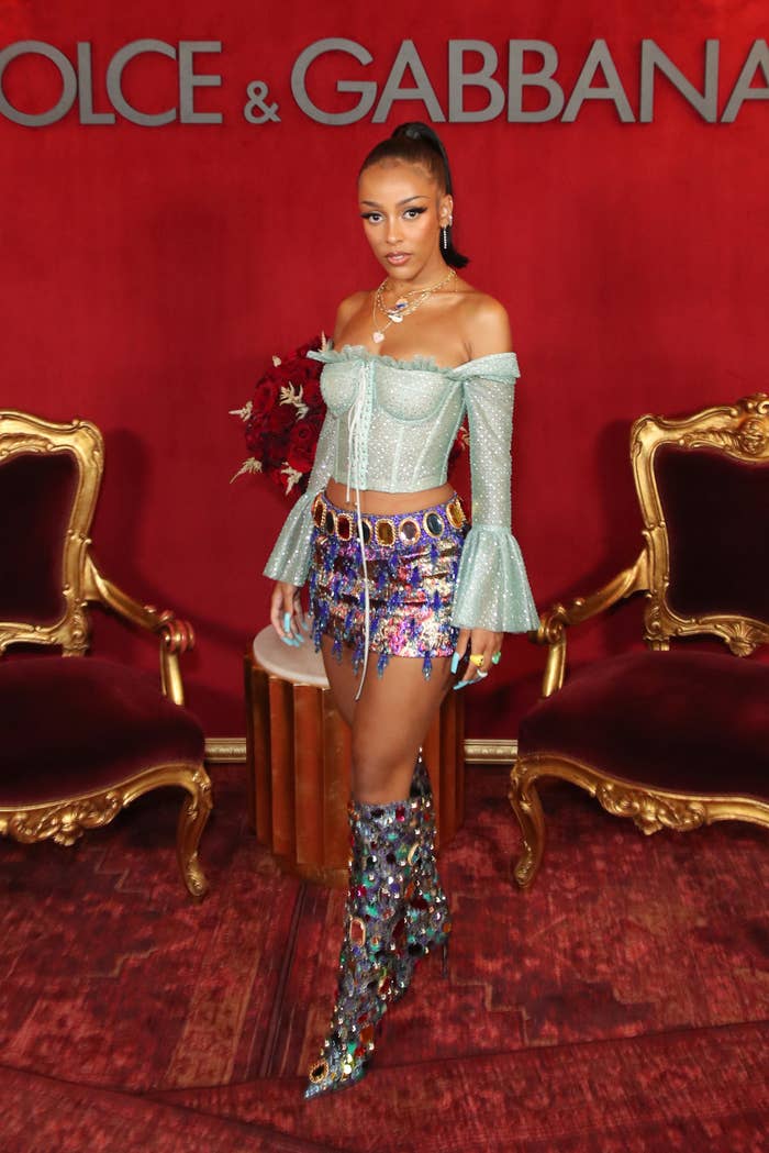 Doja Cat posing for a photo in a long-sleeved top, mini skirt, and knee-high boots at a Dolce and Gabbana event