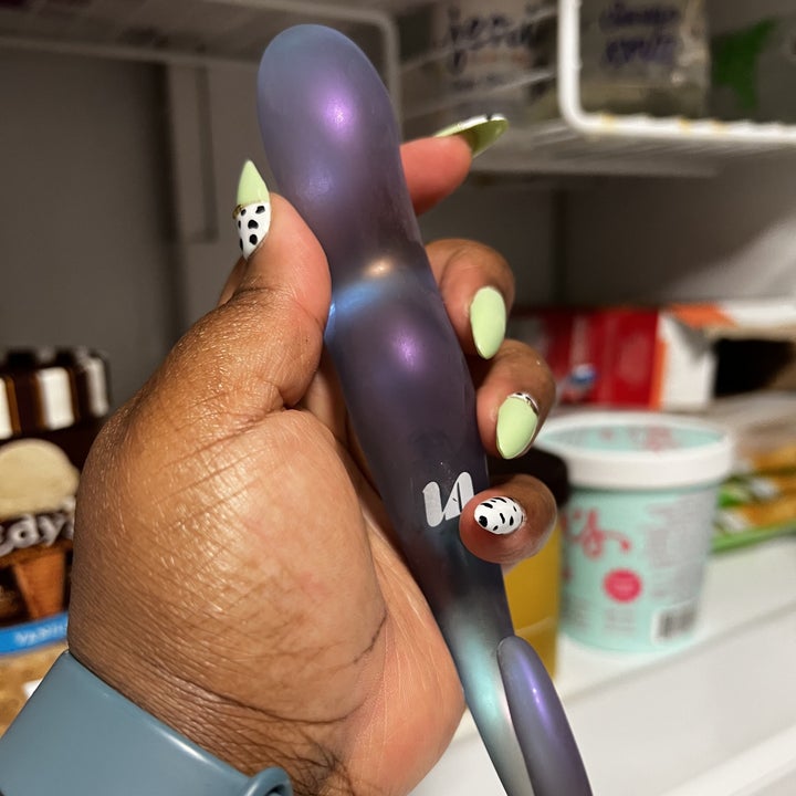 Hand holding frosted glass dildo in front of freezer filled with food