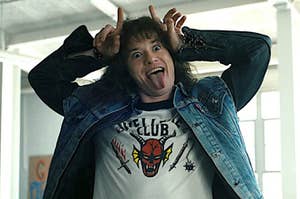Eddie Munson wears a denim jacket while making devil horns with his fingers
