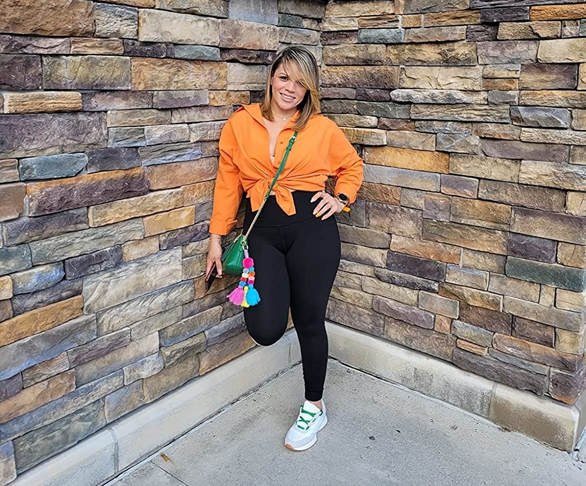 Reviewer posing in the orange top tied at the front with high-waisted leggings