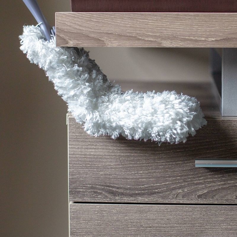 the fluffy white duster being used on a wooden dresser
