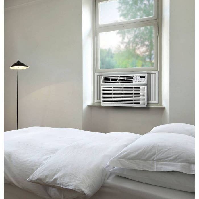 a white through-the-wall air conditioner next to a bed