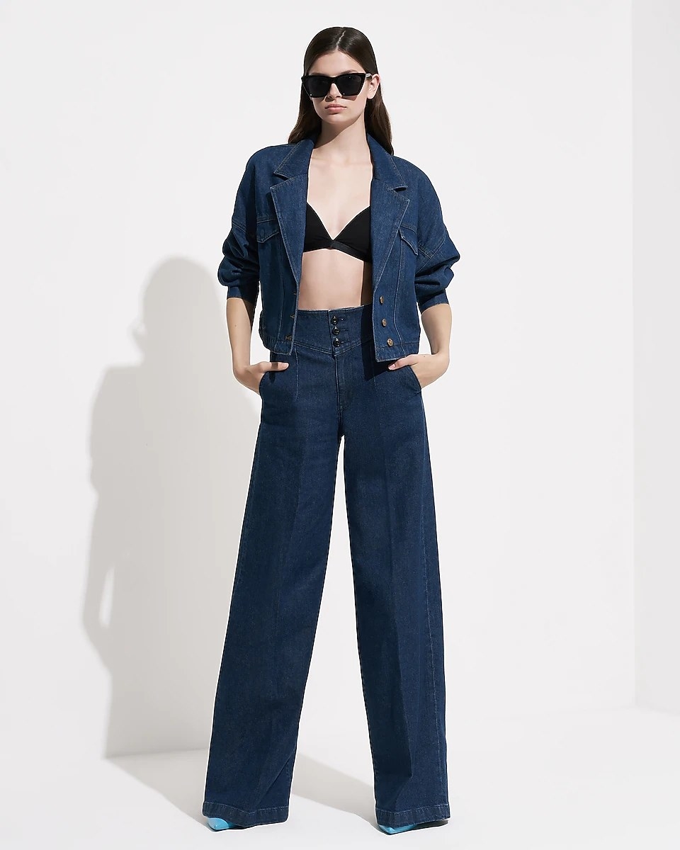 A model wearing the jeans, styled with a black bra top and an open denim blazer