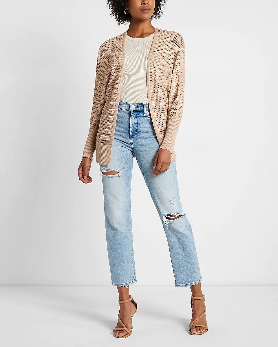 A model wearing the cardigan in the color Beige, styled over a white tee with high-waisted jeans