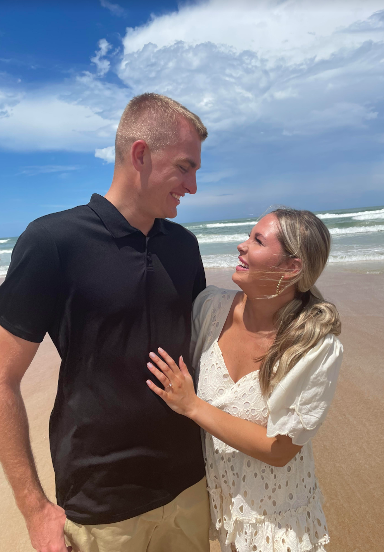 The couple look at each other happily as they stand on a beach