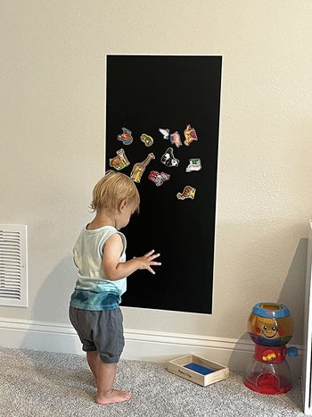 reviewer's child standing in front of the chalkboard wallpaper with animal magnets on it