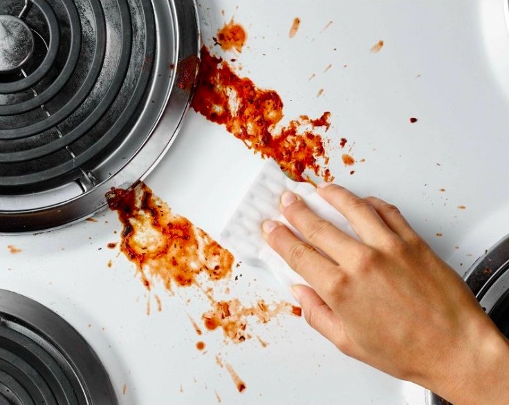 Person scrubbing red sauce splattered stove