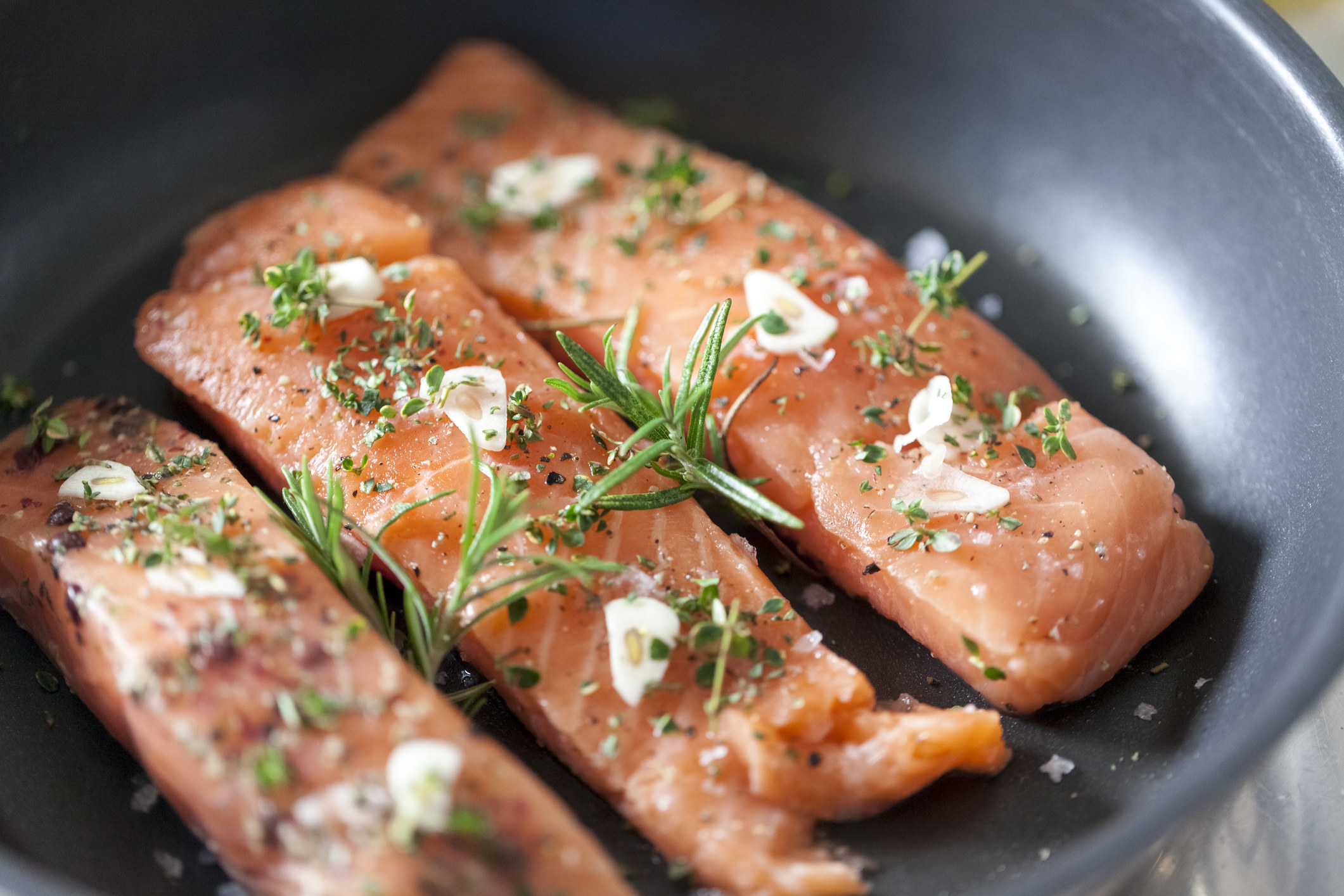 Salmon in a pan with garlic and herbs.
