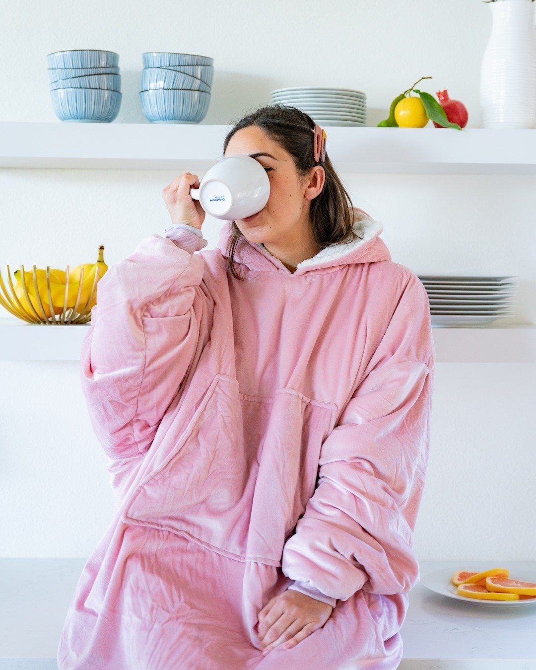 a person sipping something out of a mug while wearing the oversized hooded comfy