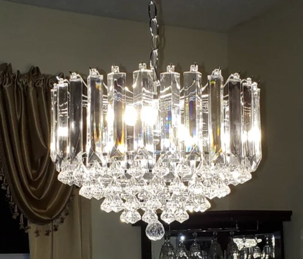 Reviewer&#x27;s photo of the chandelier hanging in dining room and glowing with elegant sparkle