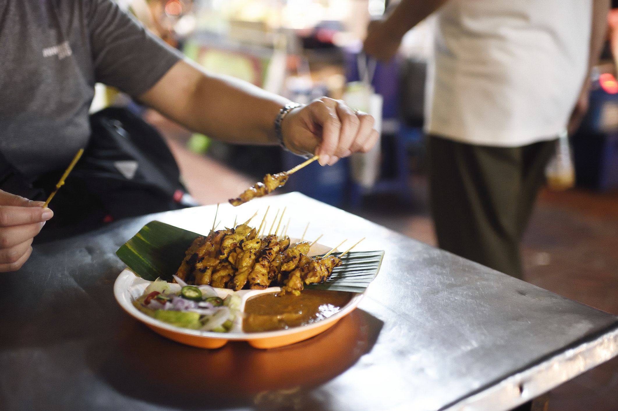 A hand picking up chicken satay street food