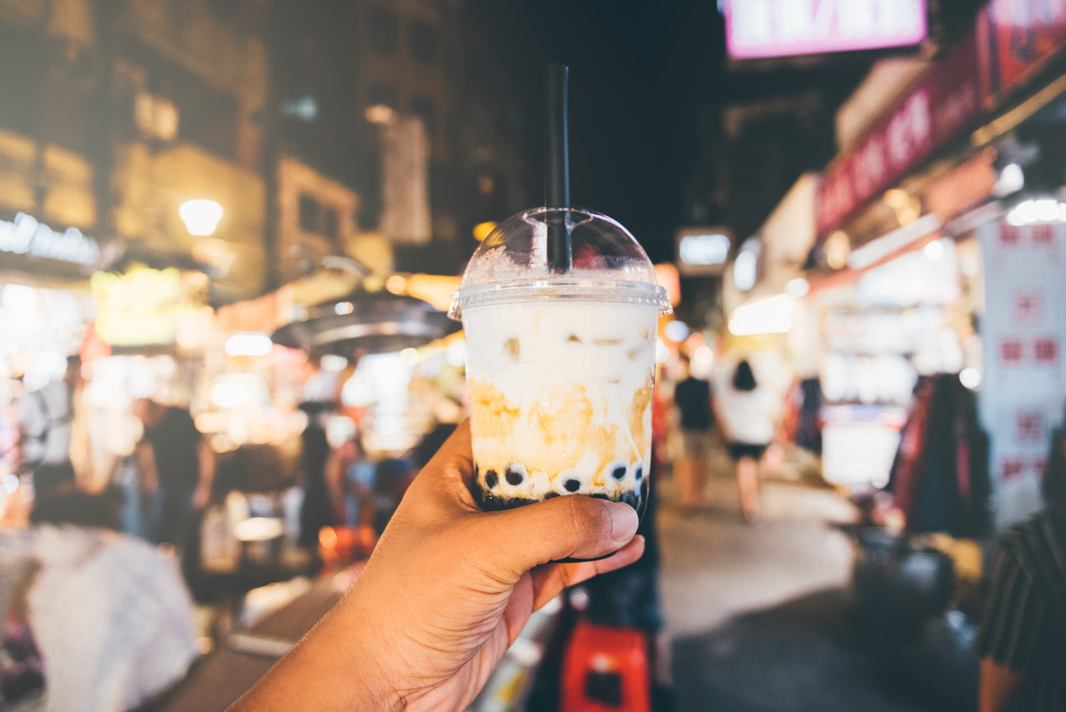 A hand holding boba tea in a night market