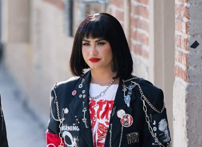 Demi seen outside building rocking a bob with bangs and wearing a ripped shirt and a jacket adorned with chains and pins