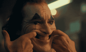 The Joker pulls his cheeks to fake a smile as he cries