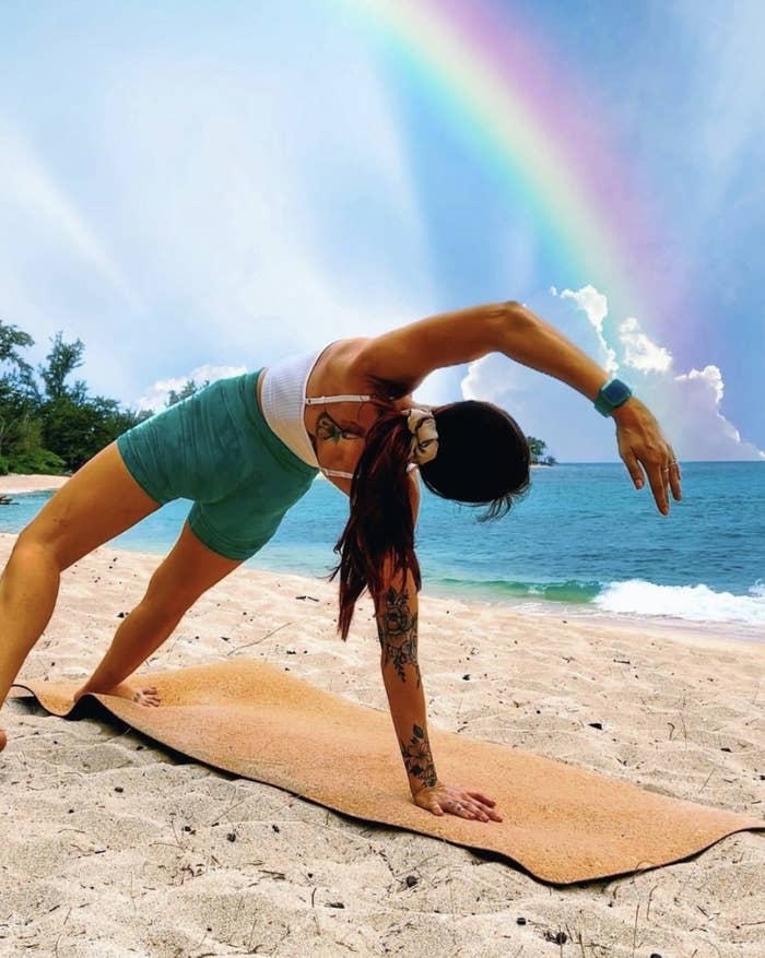Someone in open back bend pose on cork yoga mat on beach