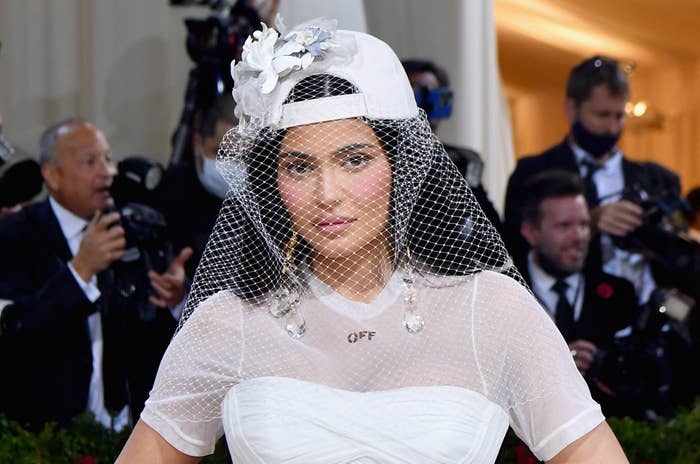 Kylie at the MET Gala wearing an short-sleeved gown and a backwards hat with a lace blusher veil over her face