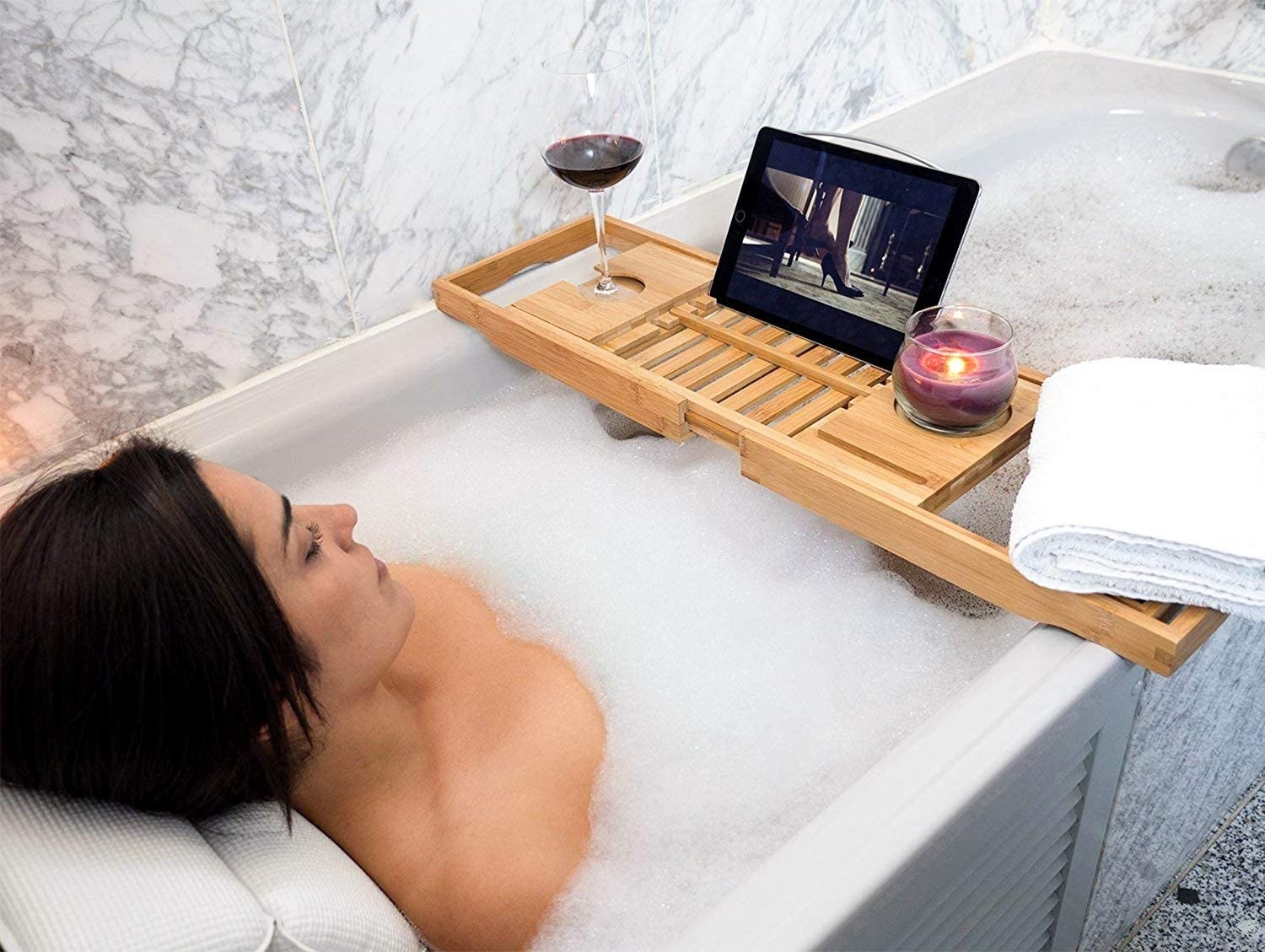 a person lounging in a tub, watching a movie from a tablet that is perched on the tub tray