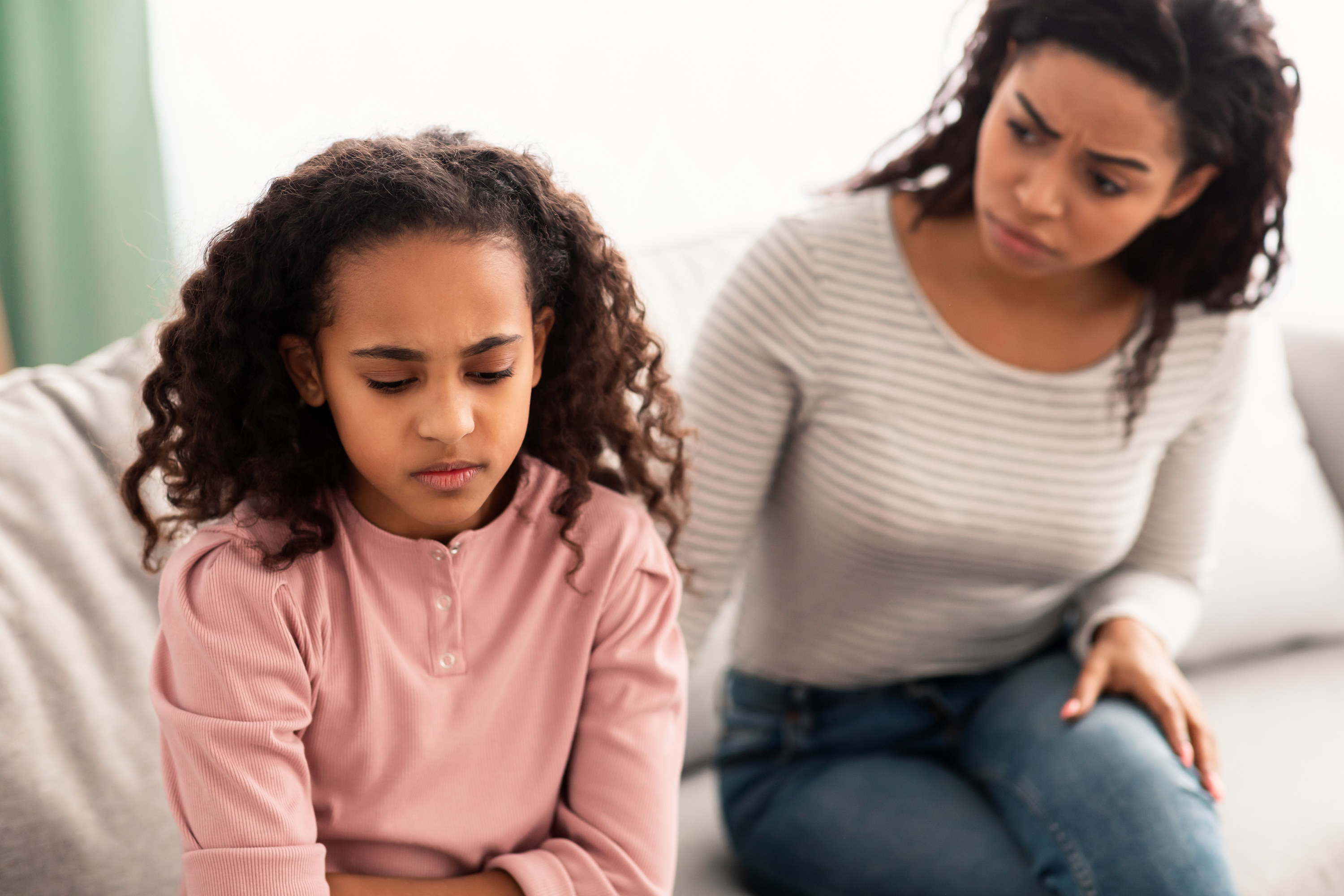 sad daughter sitting on the couch with her back to her mom