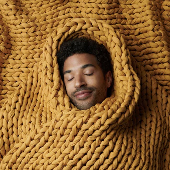 model's face exposed with entire body wrapped in large knit blanket