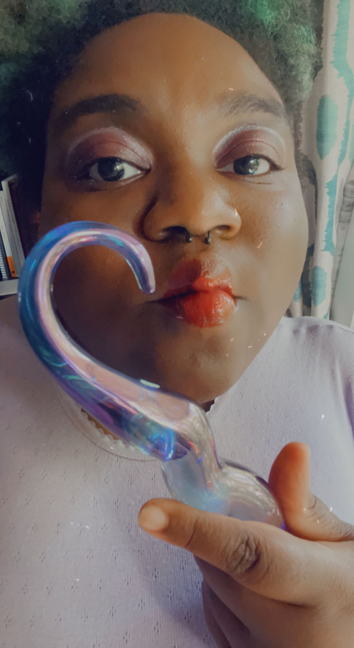 Woman pursing lips with curved handle of glass dildo near mouth