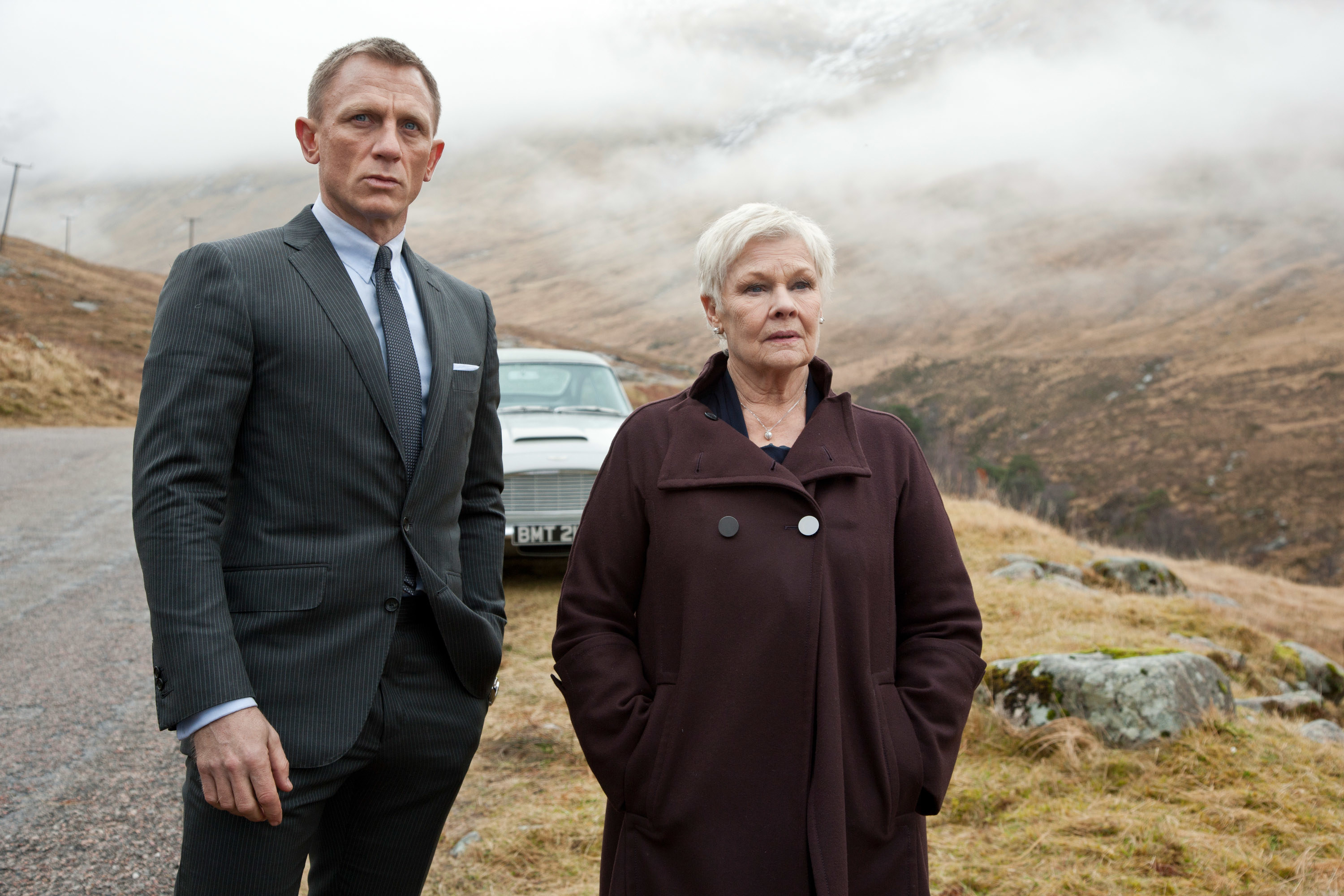 Daniel Craig and Judi Dench stand on the British countryside