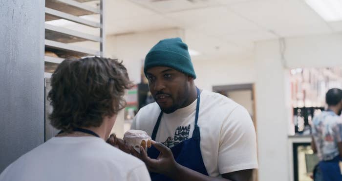 Marcus holding a donut in front of another character in the kitchen