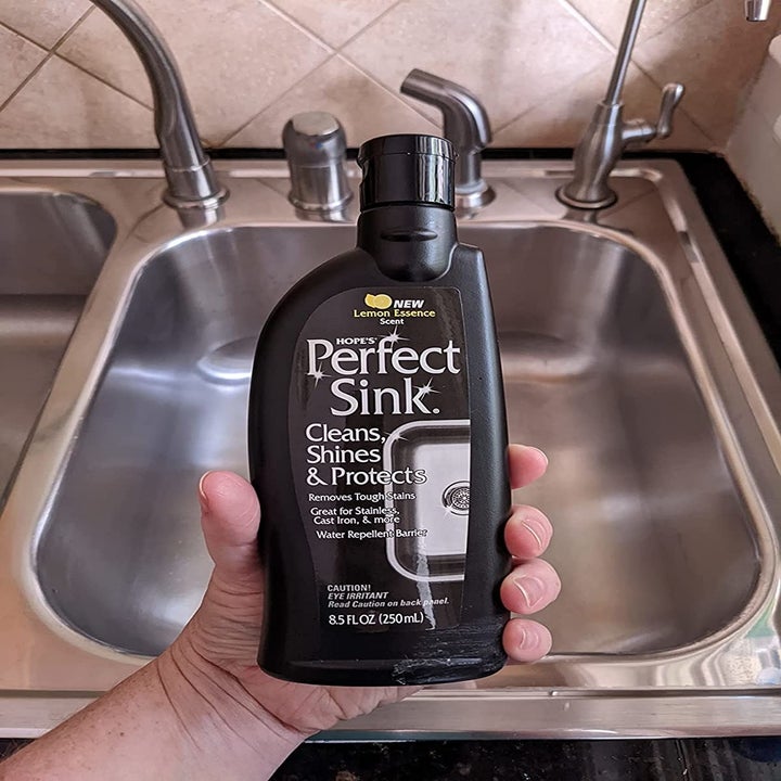 reviewer holding a bottle of the cleaner in front of a sparkling clean-looking sink
