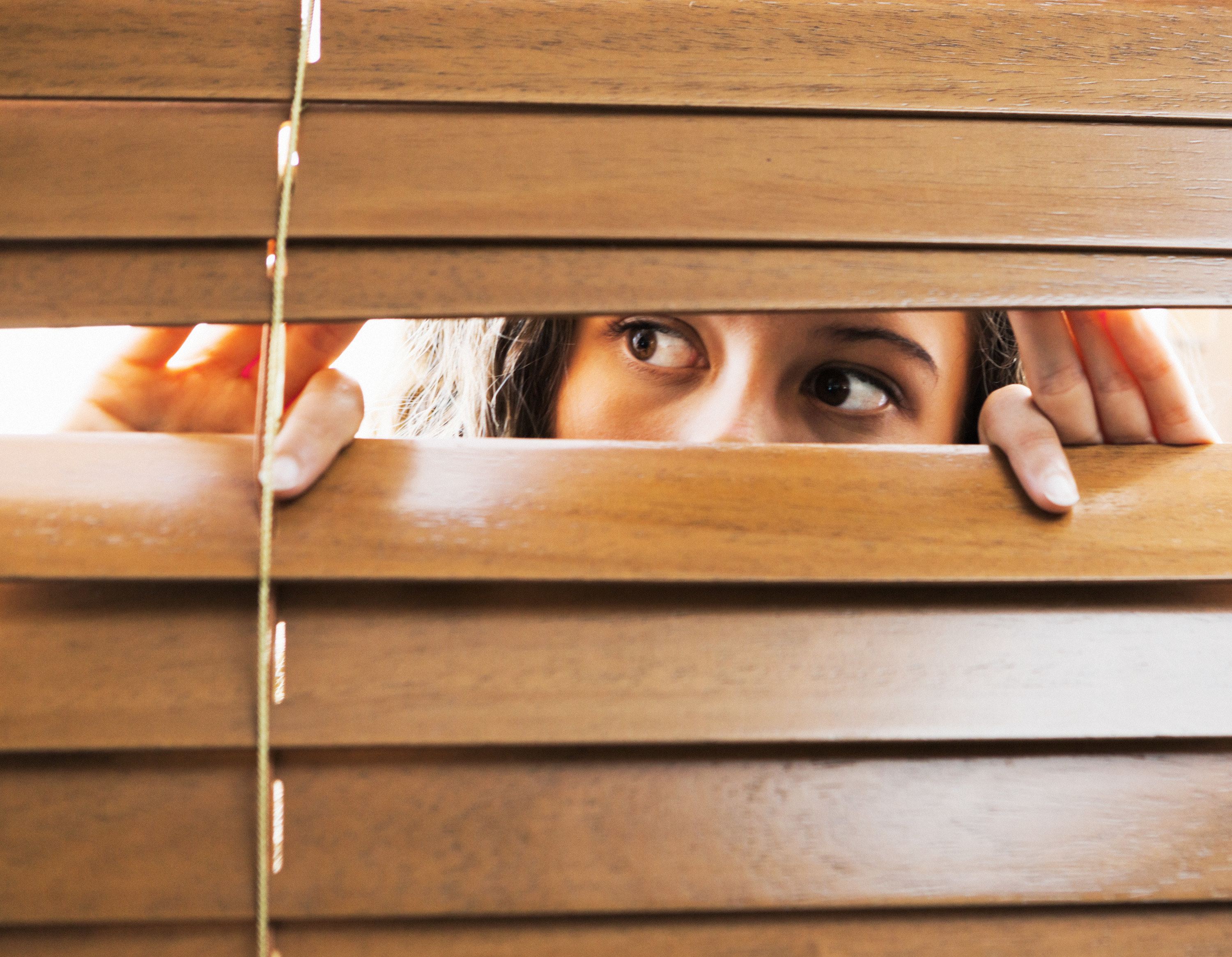 Woman looking through window blinds