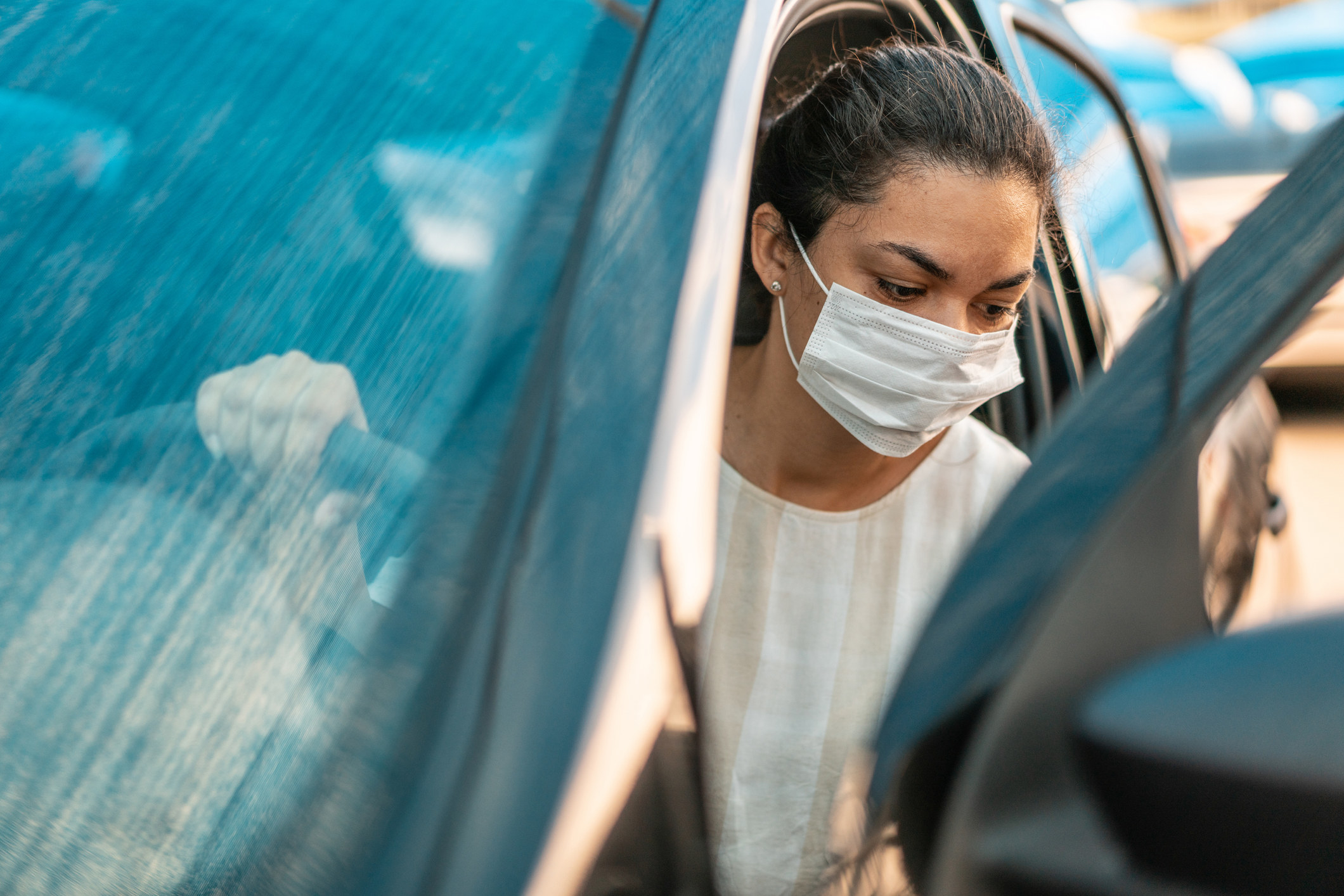 Woman wearing a surgical mask and emerging from a car