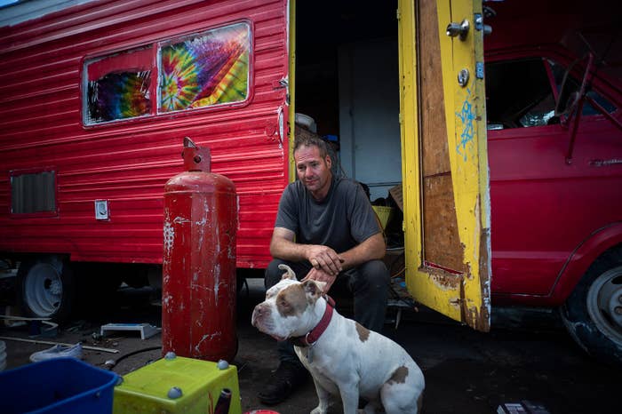 Jordan Smith sits outside his red RV next to his spotted dog