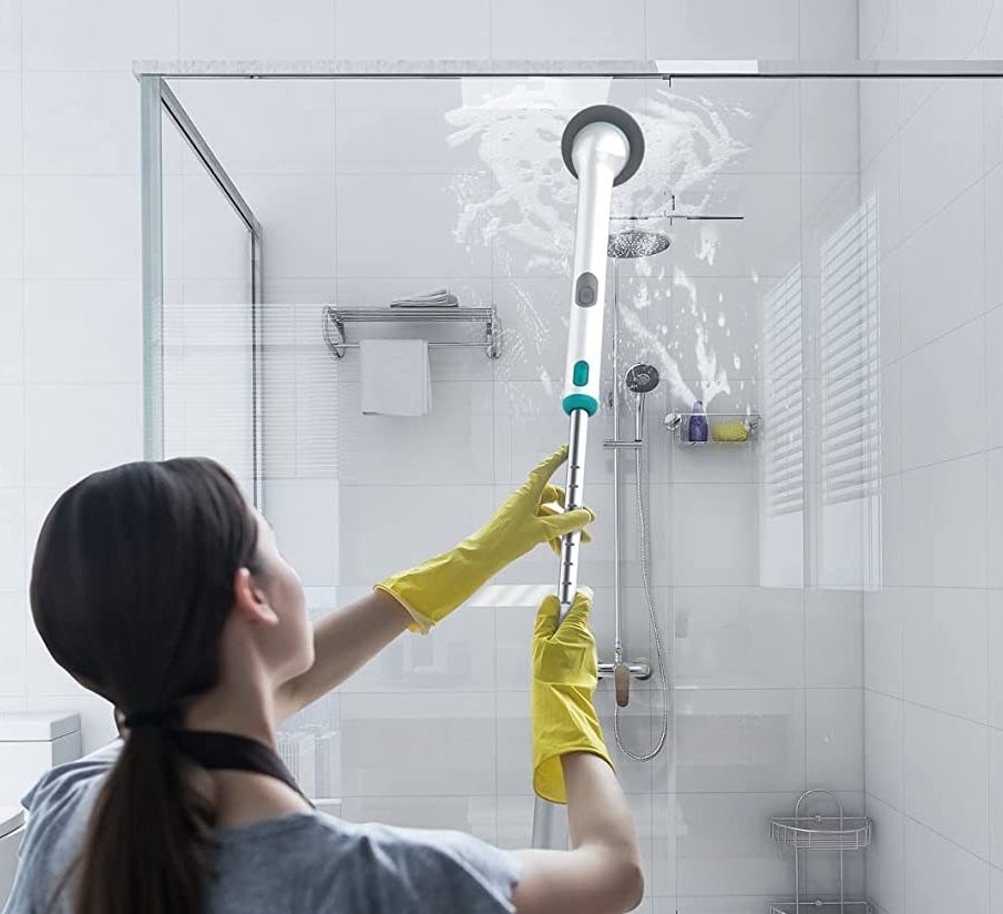 a person using the scrubbing want to clean the top of a shower