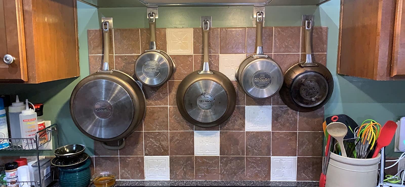 Reviewer&#x27;s kitchen pans and pots are shown hanging from the hooks in their kitchen