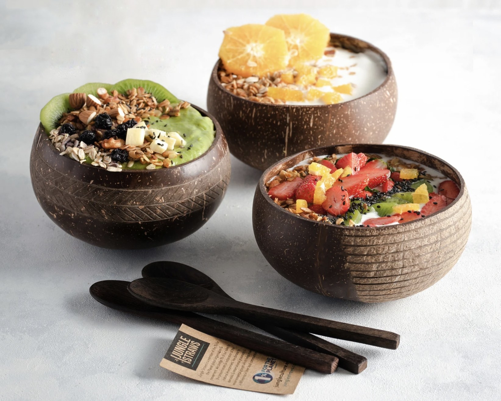 Three of the coconut bowls each filled with a smoothie bowl with spoons resting on table