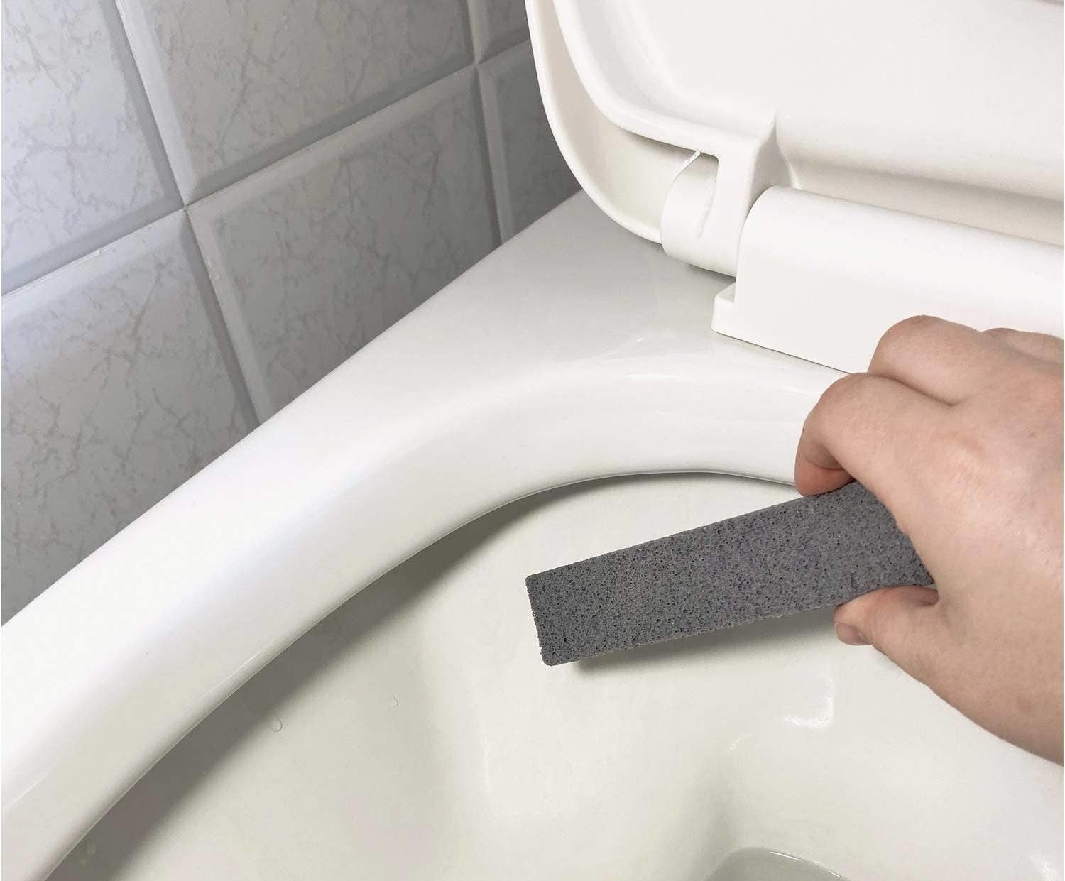 a person holding a pumice want above a toilet bowl
