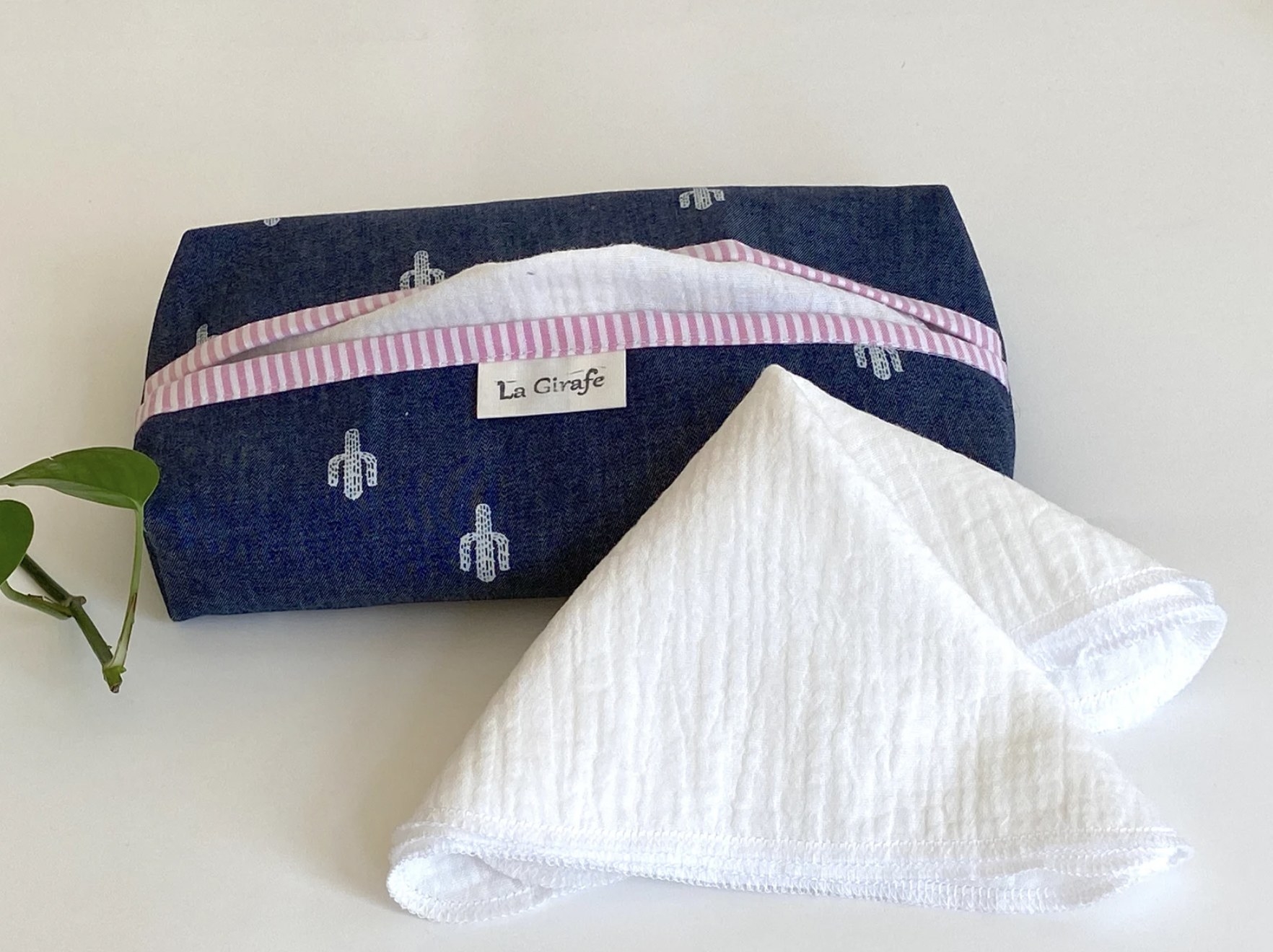 The denim tissue box with cactus print and pink striped trim with one cotton reusable tissue pulled out