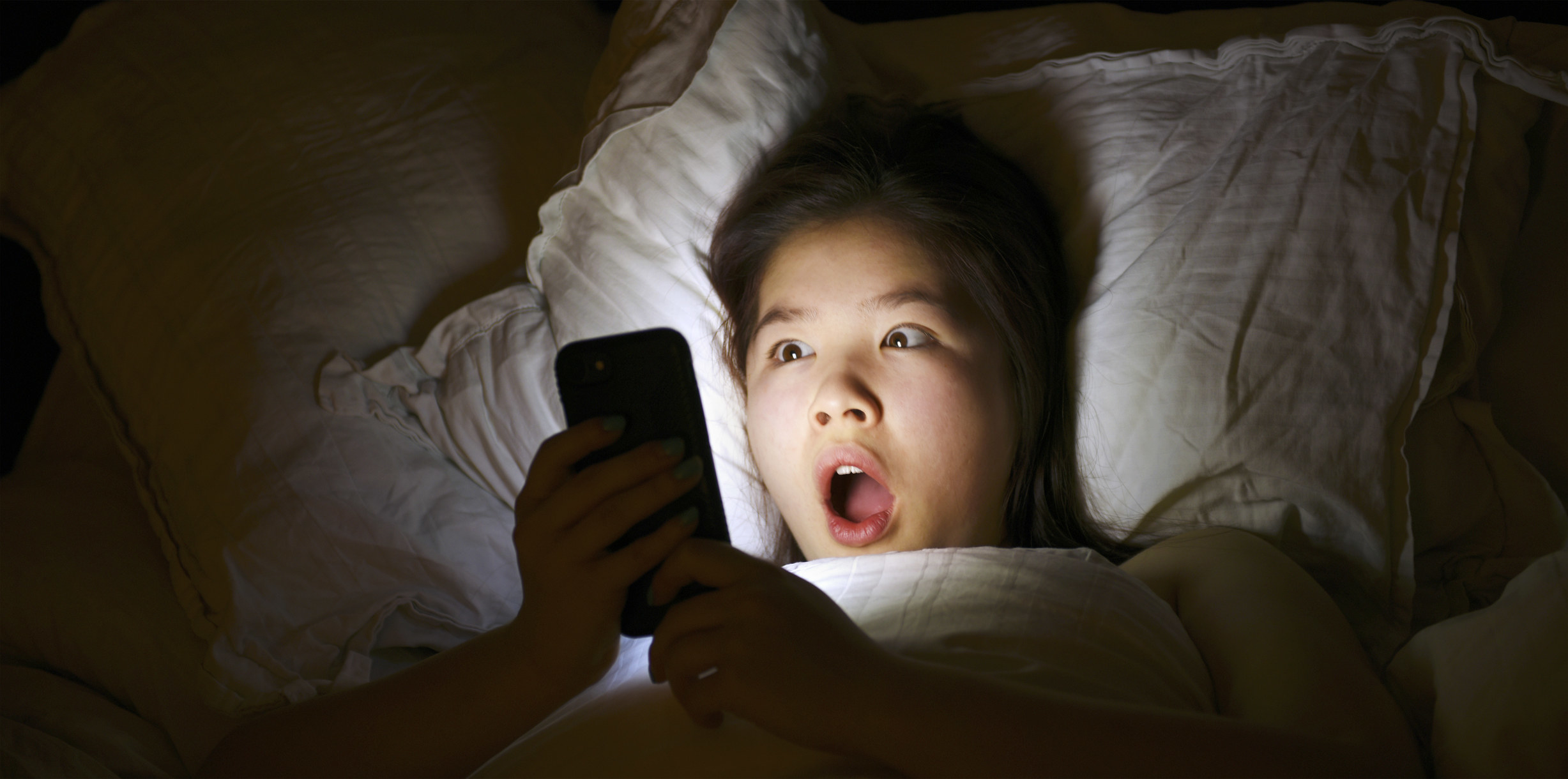 a person with a shocked expression looking at a phone in bed