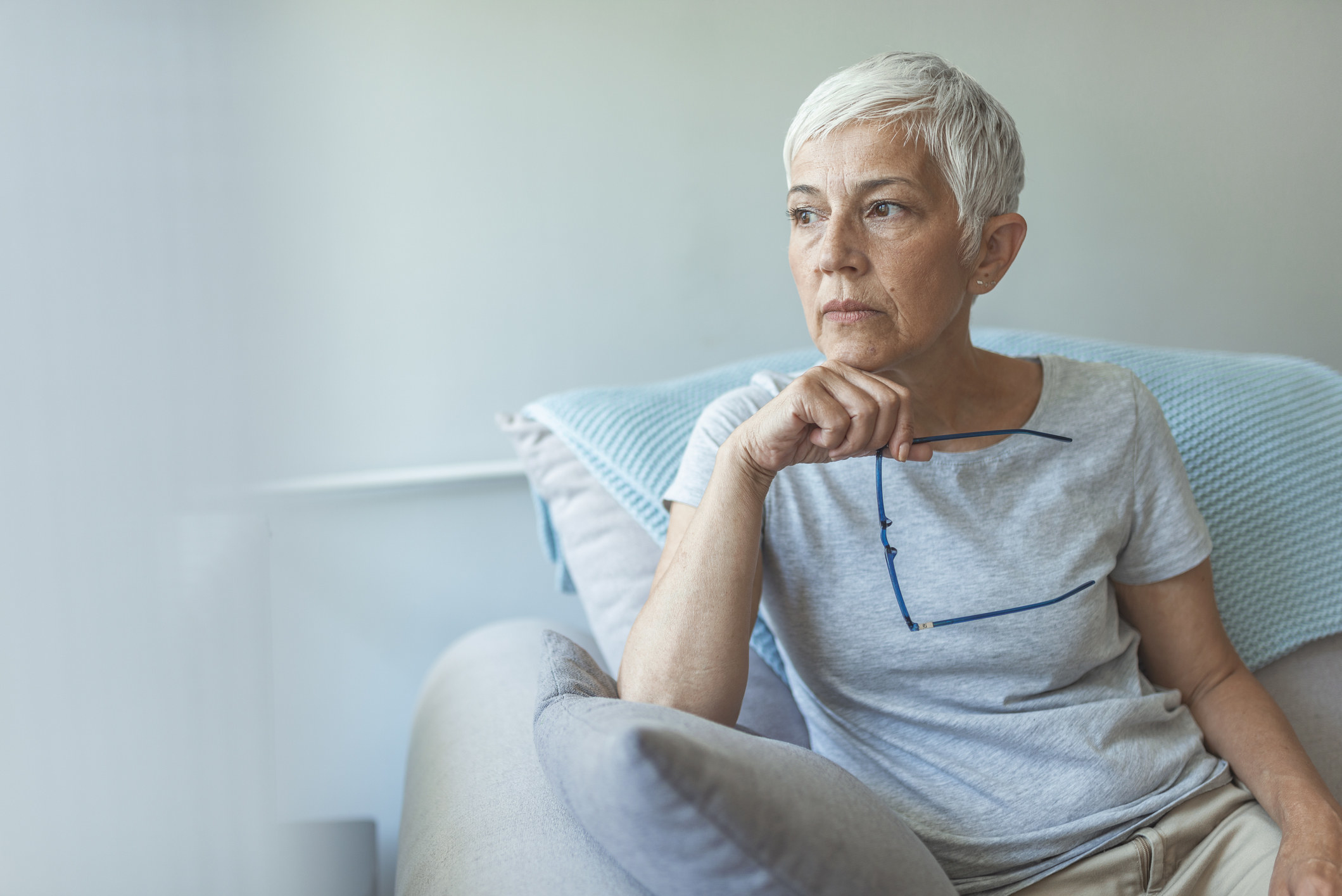 An older woman sitting on a couch and looking thoughtful
