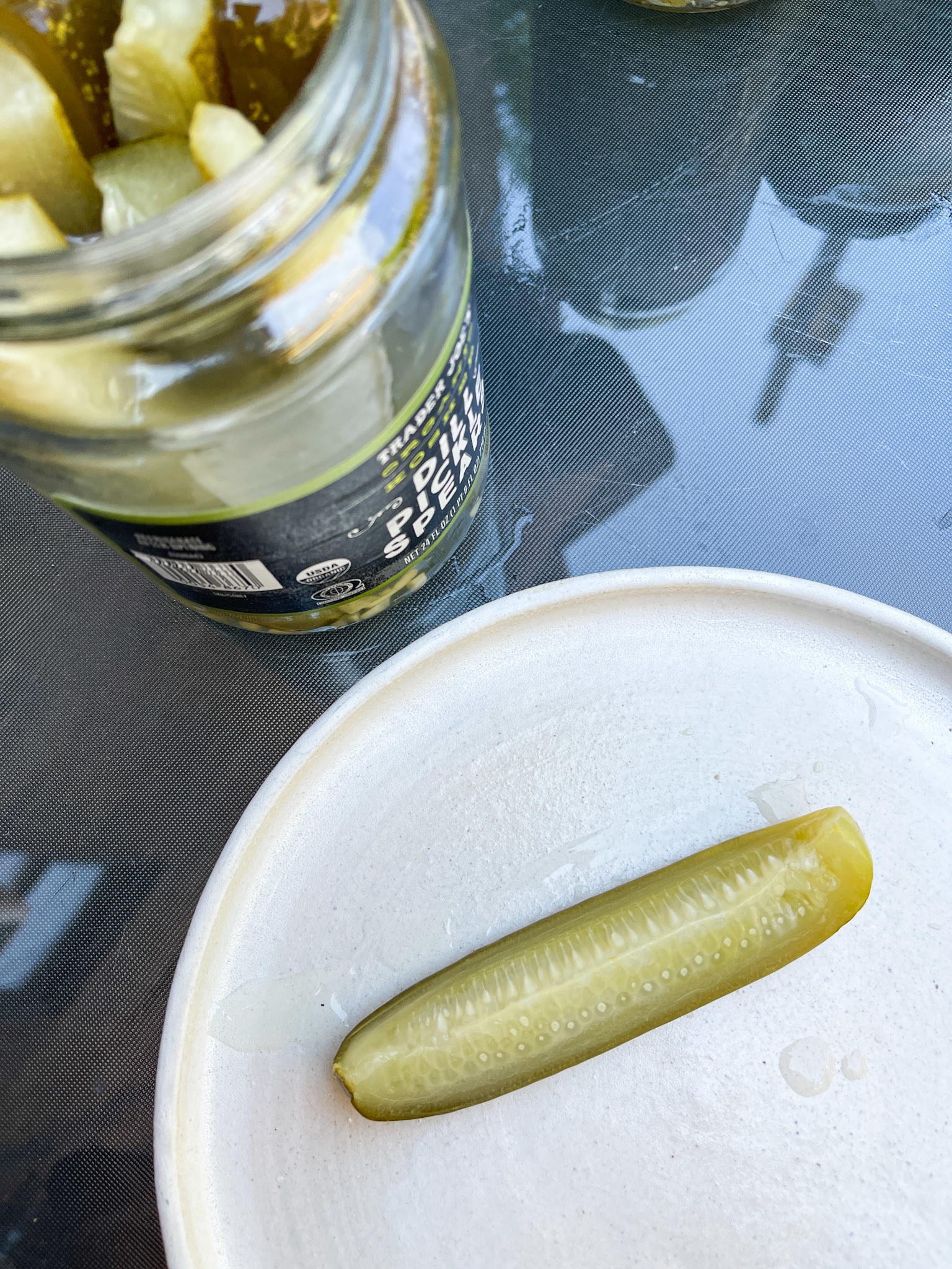 Jar of pickles open with one pickle on a plate, indicating a food topic related to pickles