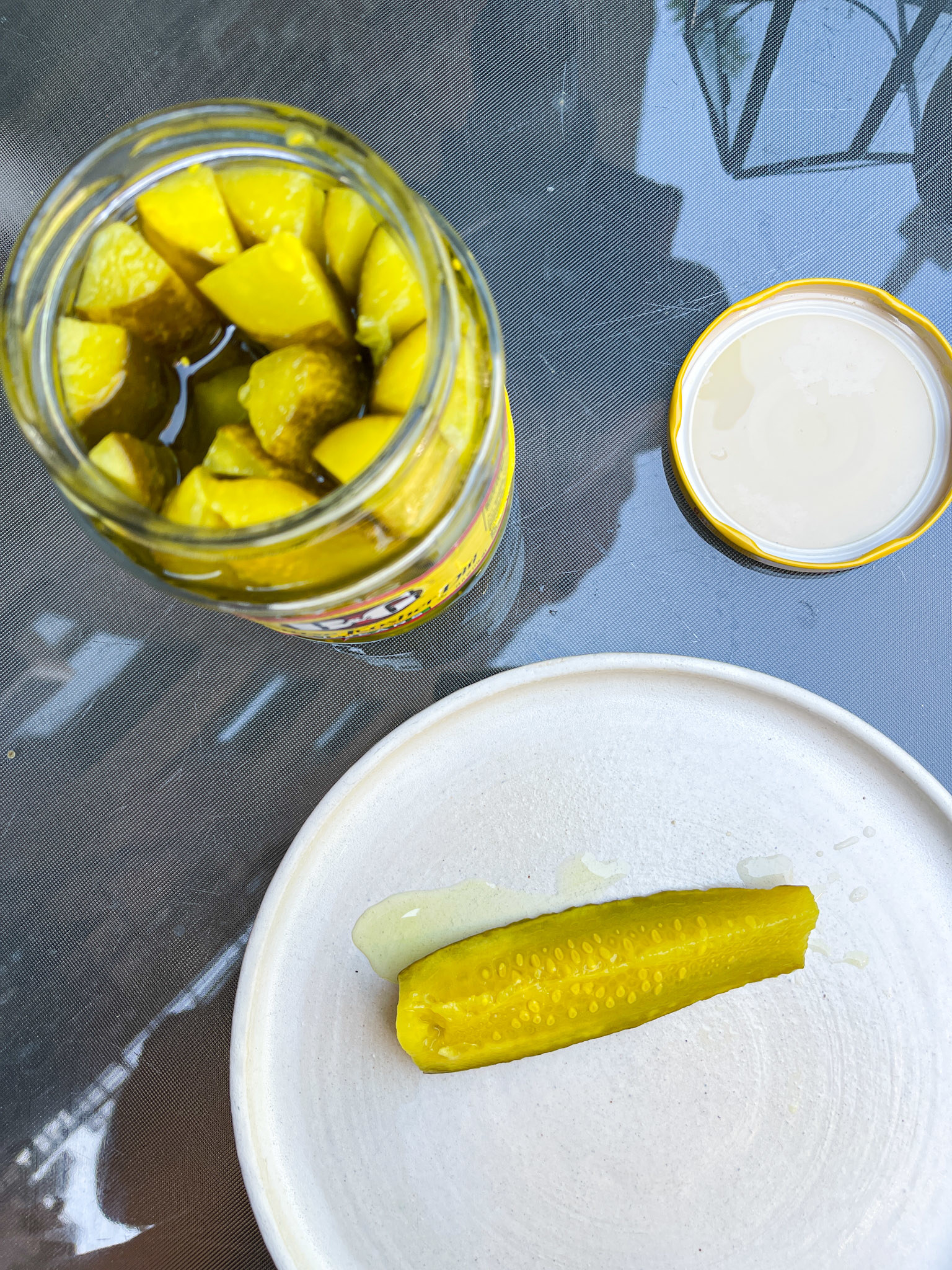 Top view of an open pickle jar with pickles and a single pickle on a plate