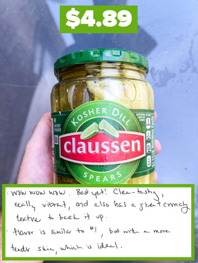 Hand holding a jar of Claussen Kosher Dill pickles with a price tag, annotated with positive handwritten taste review