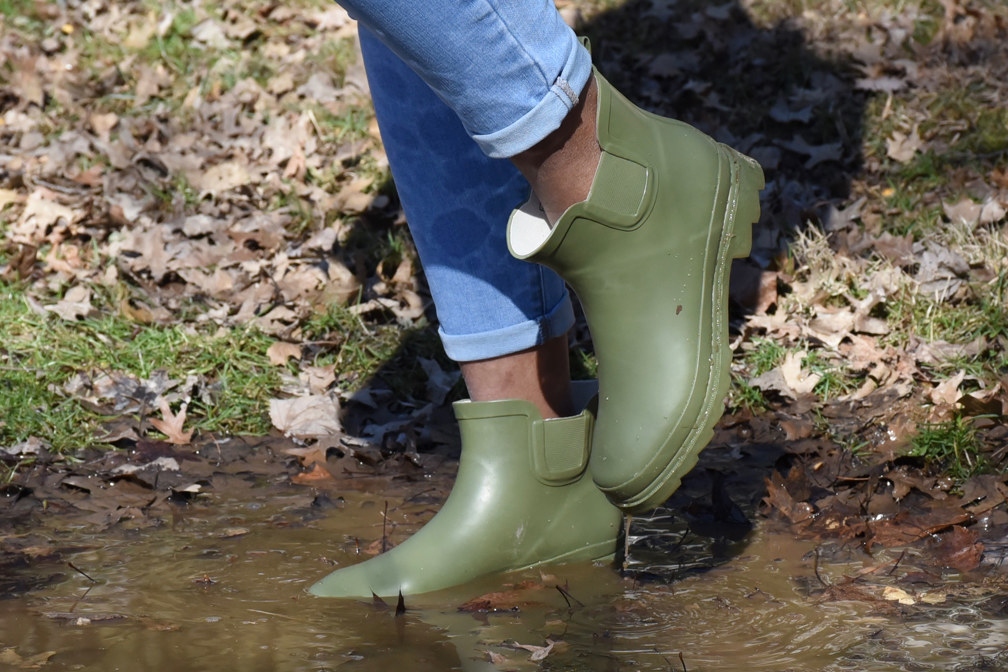 a model wearing the green rain boots and walking in a puddle