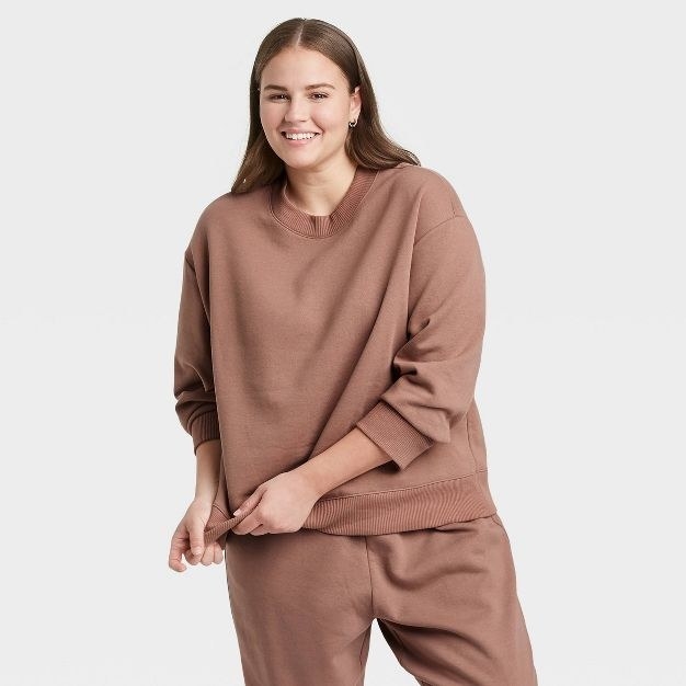 The model wears the sweatshirt and sweatpants in brown