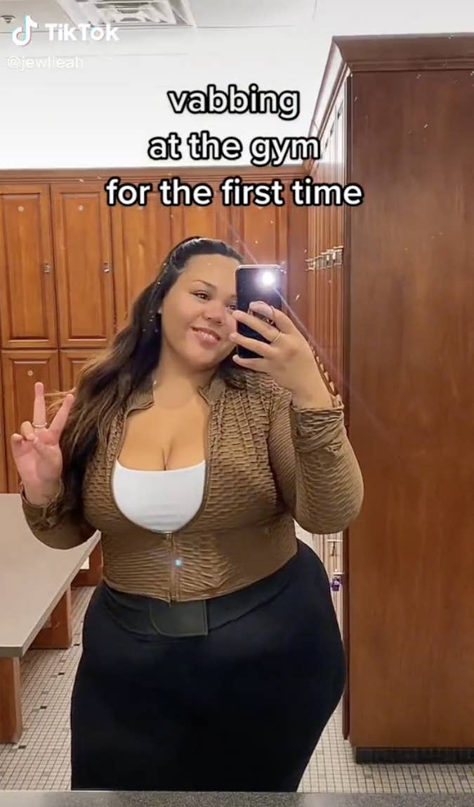 TikTok screenshot of woman taking a selfie in a bathroom with the caption &quot;vabbing at the gym for the first time&quot;