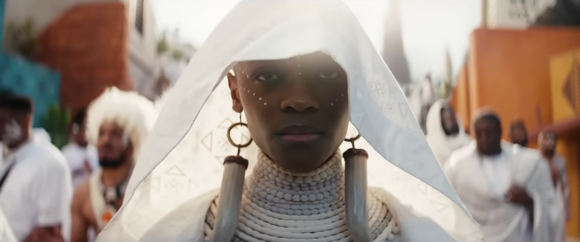 Shuri wearing all white as she walks as part of a procession
