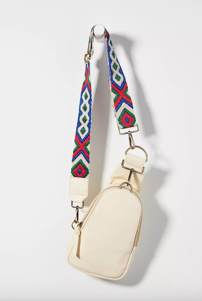 Cream colored cross body bag with blue, green, and red embroidered patterned strap